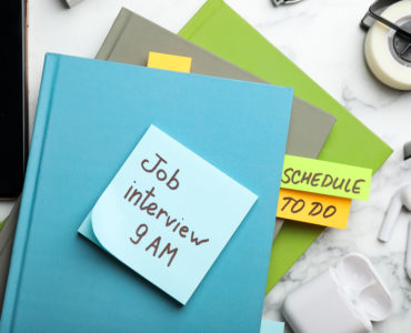 Reminder note about job interview and stationery on table, flat lay