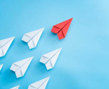 Leadership concept with red paper plane leading among white on blue background