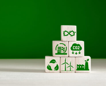 Circular economy and climate change concept. Business and environment sustainable development. Stacked wooden cubes with eco infinity and environment sustainable symbols on green background.