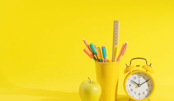 stationery, apple and retro alarm clock on a bright yellow background