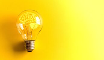 Light bulb with brain-shaped filament glowing against a yellow background, symbolizing creativity and innovation.