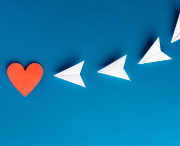 Focus, assertiveness, work yourself concept. Paper heart shape with airplane on blue background
