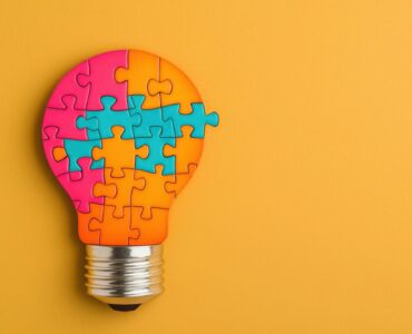 Solving a Puzzle with a Glowing Idea, Colorful puzzle light bulb on yellow background.